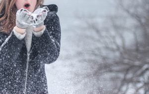 Frau steht im Schnee und pustet in ihre Hände